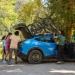 Blue 2027 Ford Mustang Mach-E Trail with a bike being loaded onto its roof
